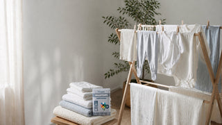 Neutrale babykleding en katoenen wasgoed op een houten droogrek bij het raam