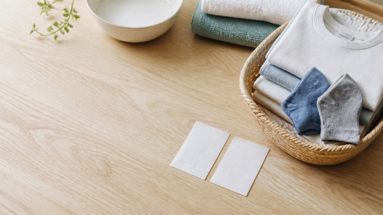 Twee witte wasstrips naast een mand met lichte was op een houten tafel